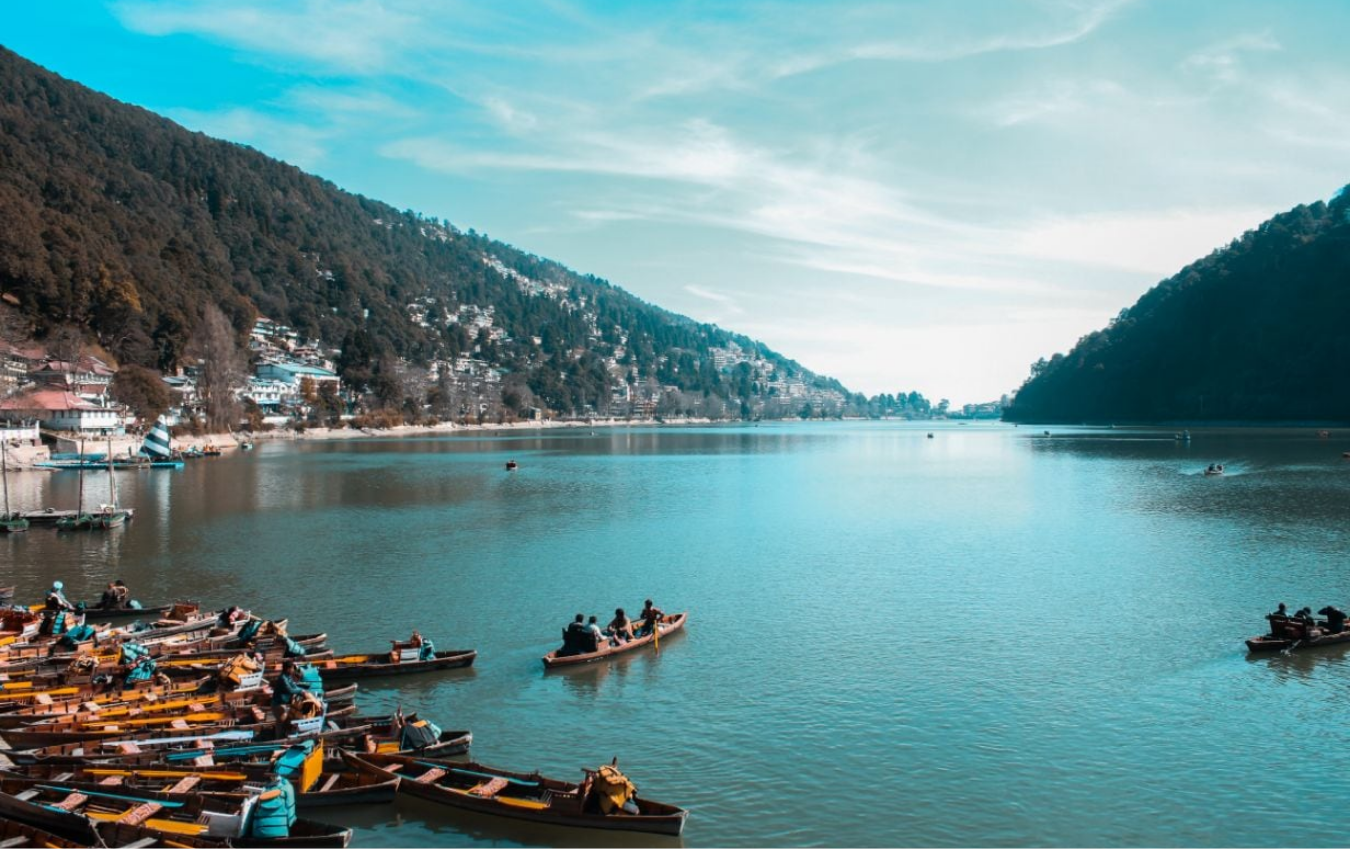 Wooden boats moored on a still Kumaon lake below forested hills